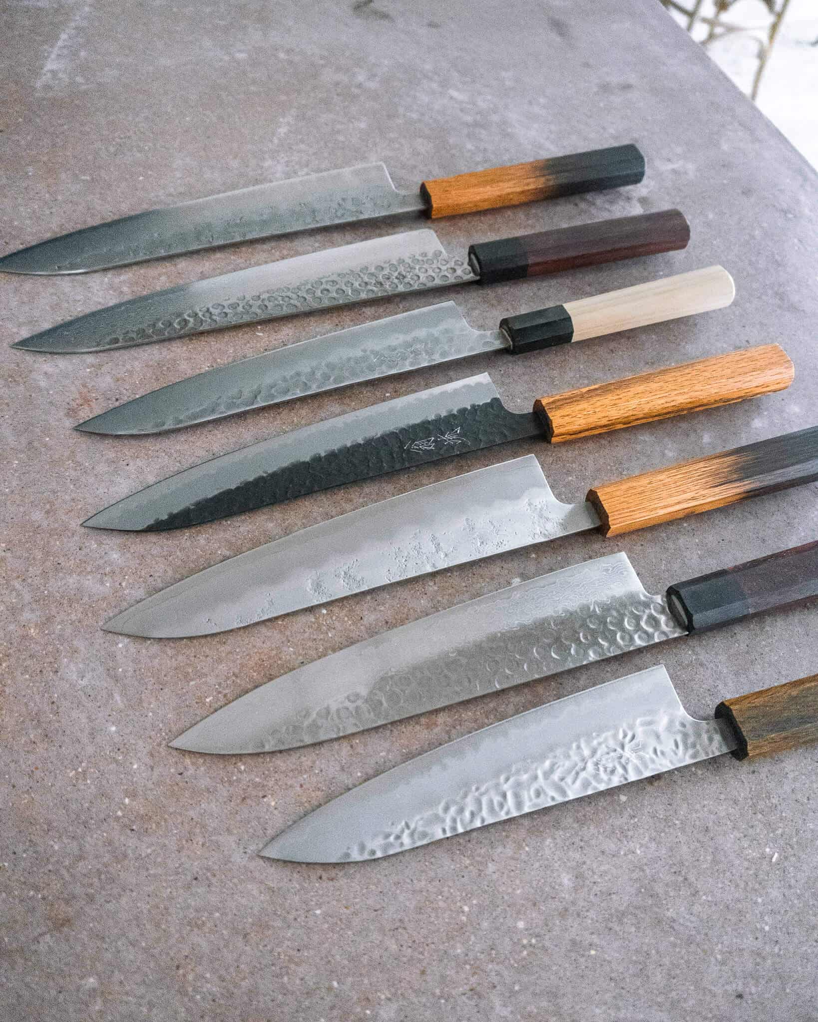 All purpose Japanese chef knives, known as Gyutos, lined up on a concrete countertop