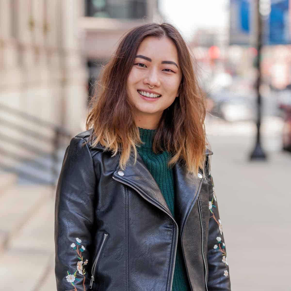 Woman wearing a black leather jacket with floral embroidery on a city street.