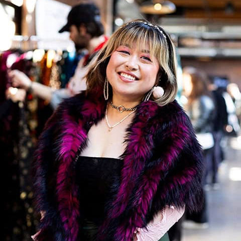 Woman wearing a dark purple fur coat in an indoor setting with blurred background