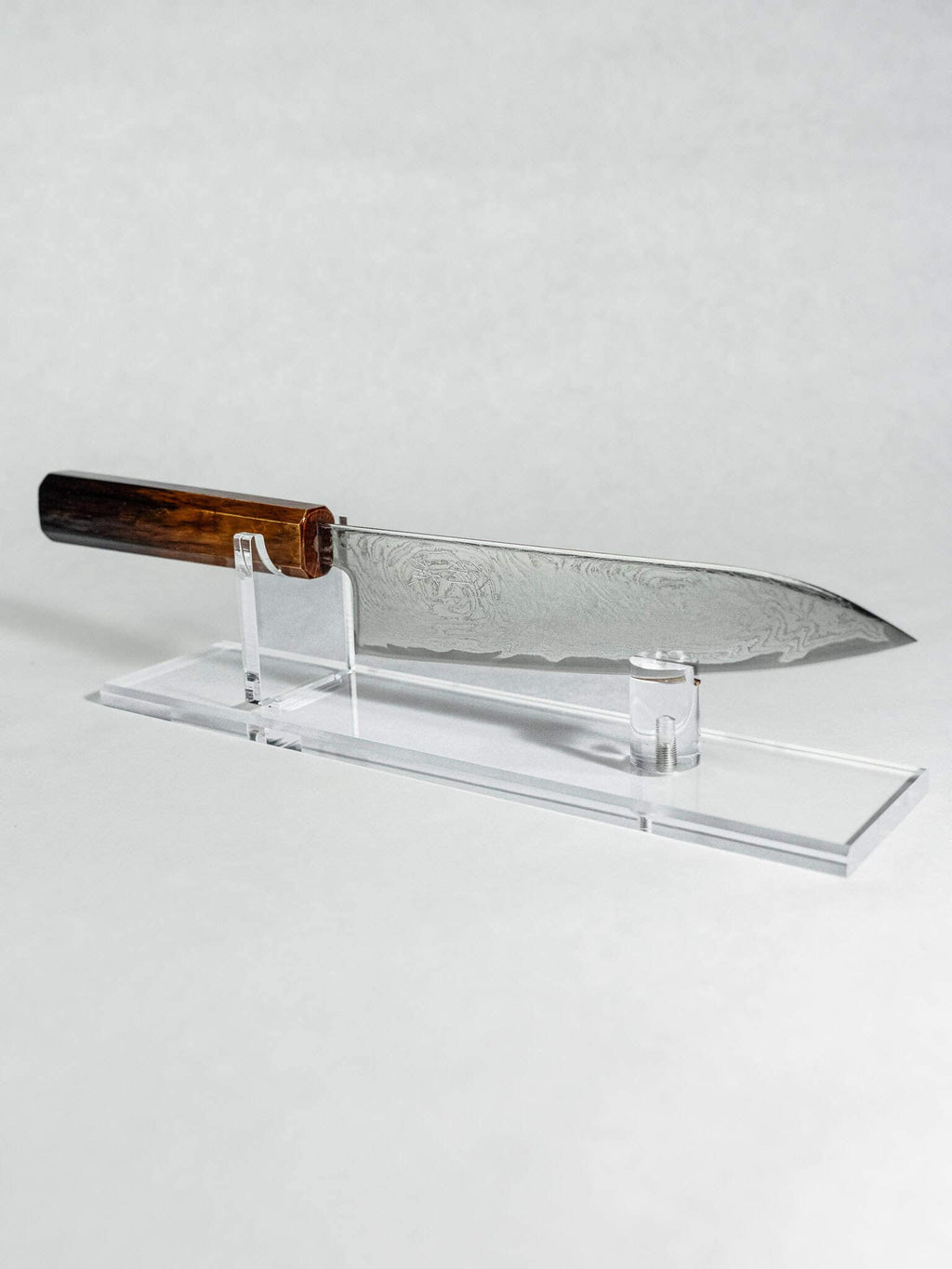 Sleek knife with a wooden handle on an acrylic stand against a white background. OUL AUS-10A Damascus Gyuto handcrafted in Sakai, Japan