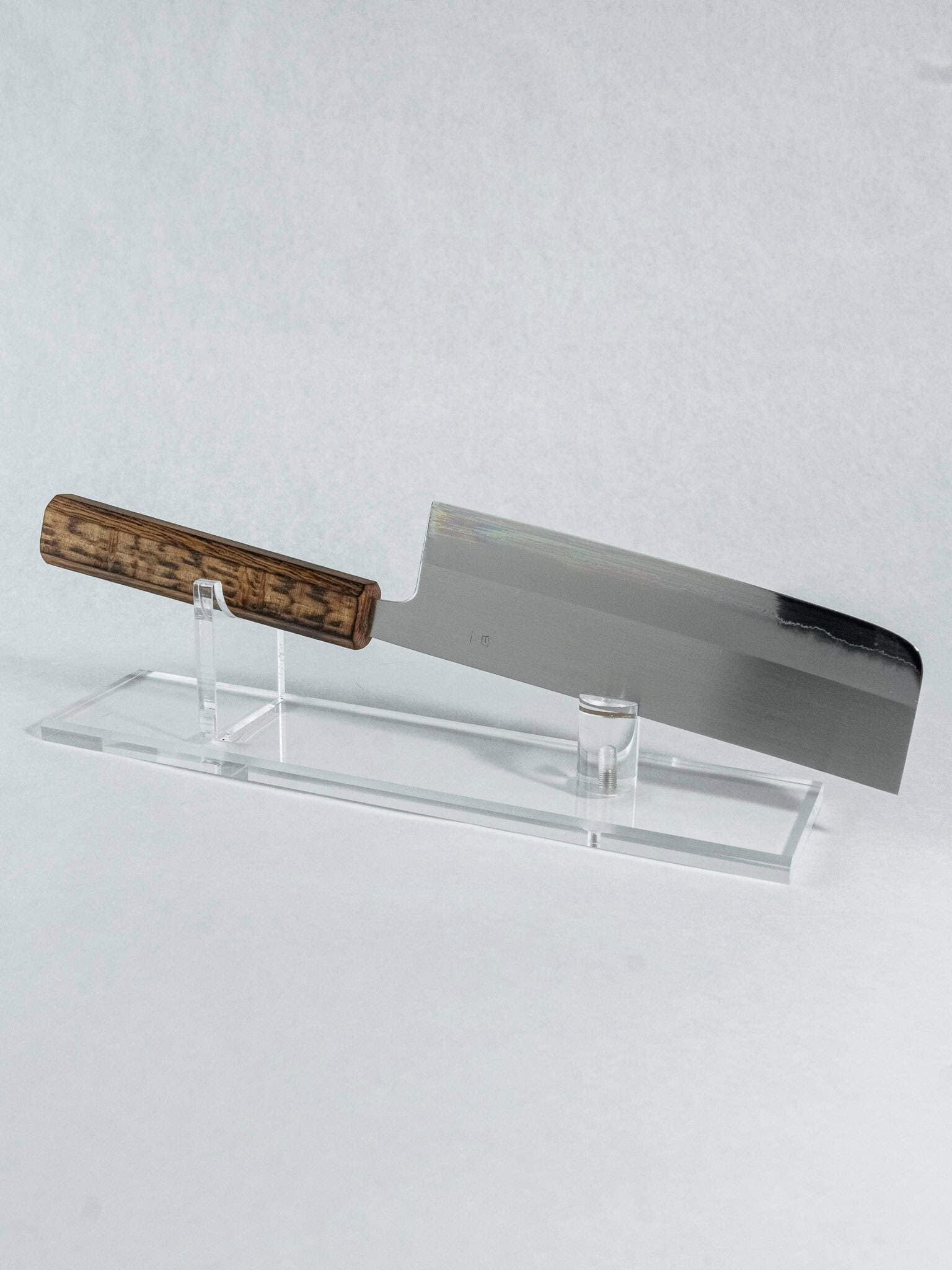 Nakiri knife with wooden handle on a clear stand against a light gray background