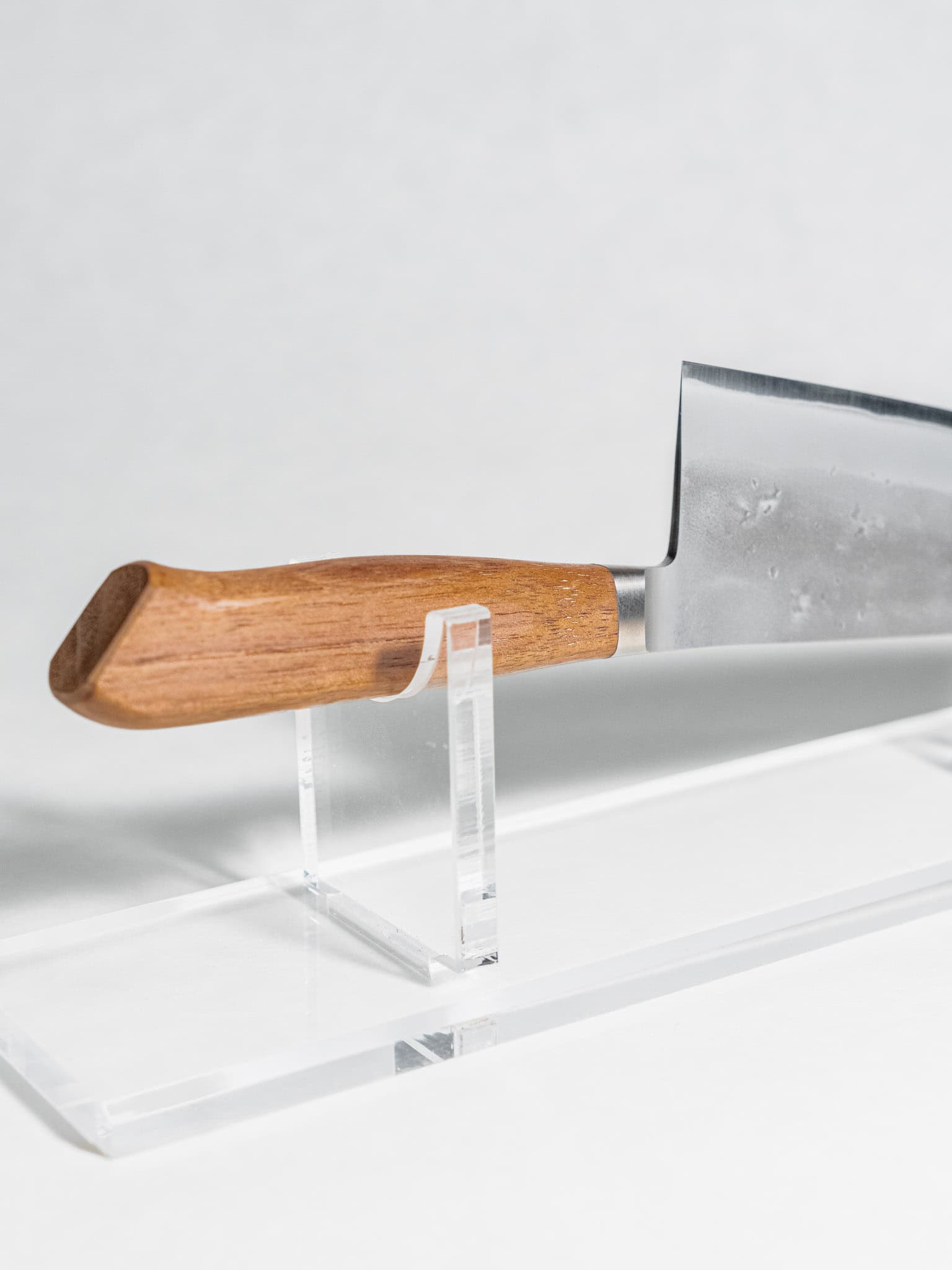 Japanese knife with walnut handle on a clear stand against a white background