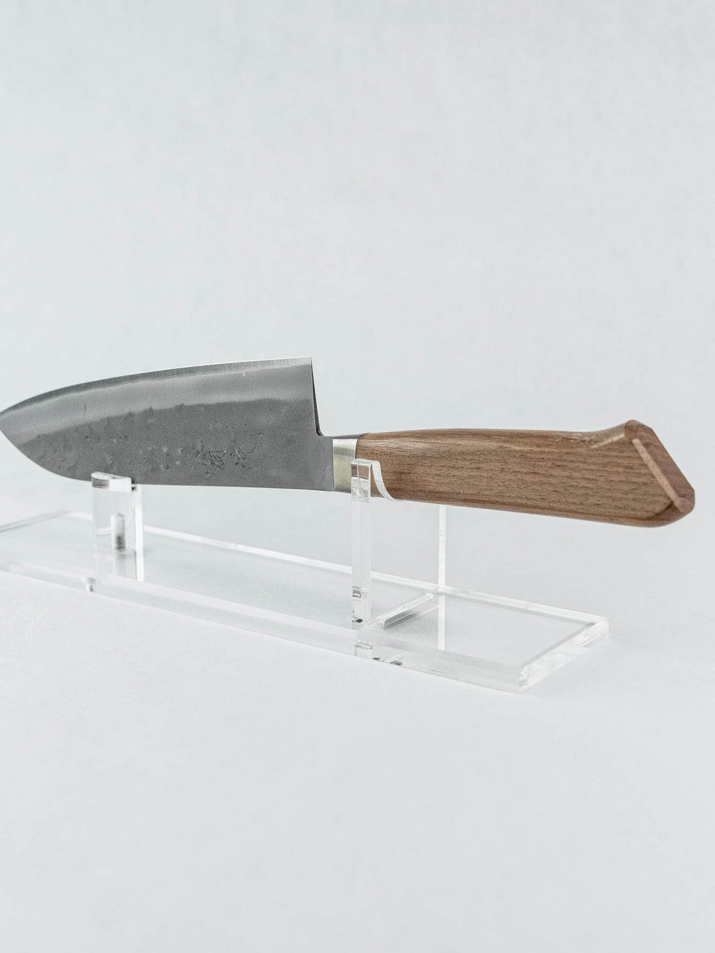OUL chef knife with a wooden handle on a clear stand against a white background