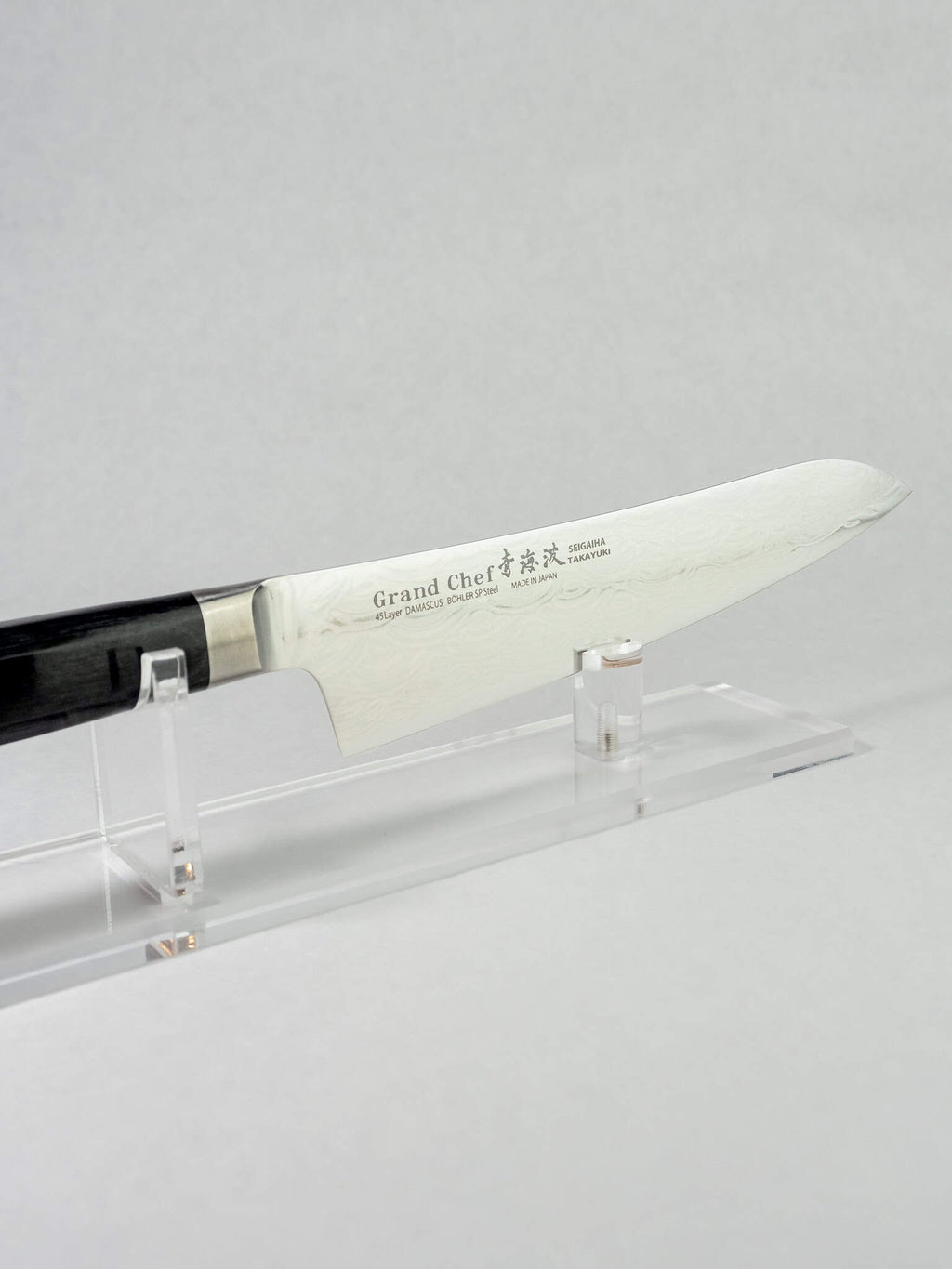 Chef's knife with 'Grand Chef' branding on a clear stand against a gray background.