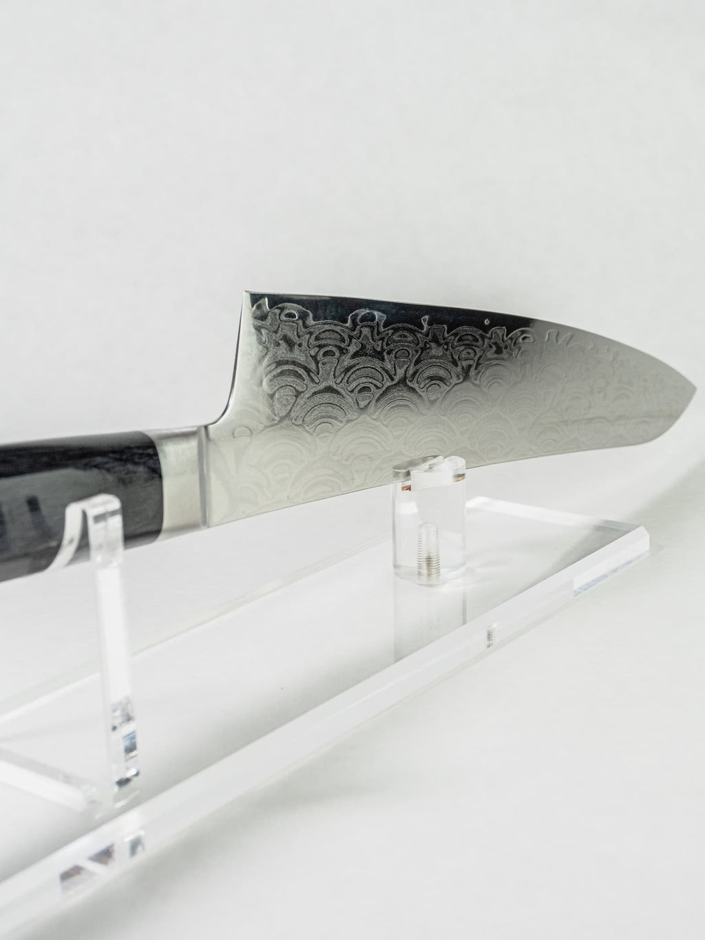 Damascus knife with stainless blade on a white stand against a white background