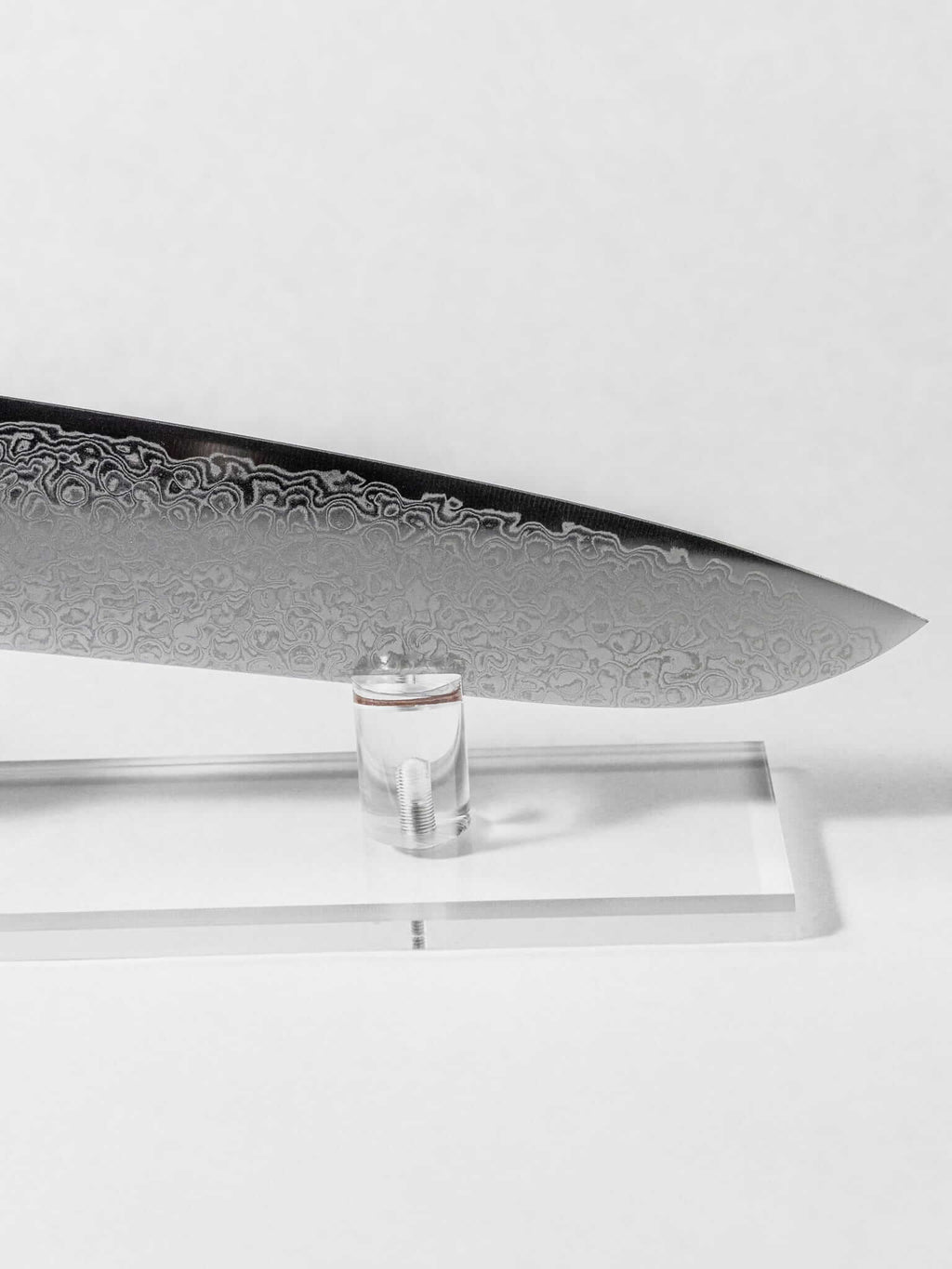 Close up of the stainless Damascus cladding pattern detail. Sharp tip of the Santoku against a white background.