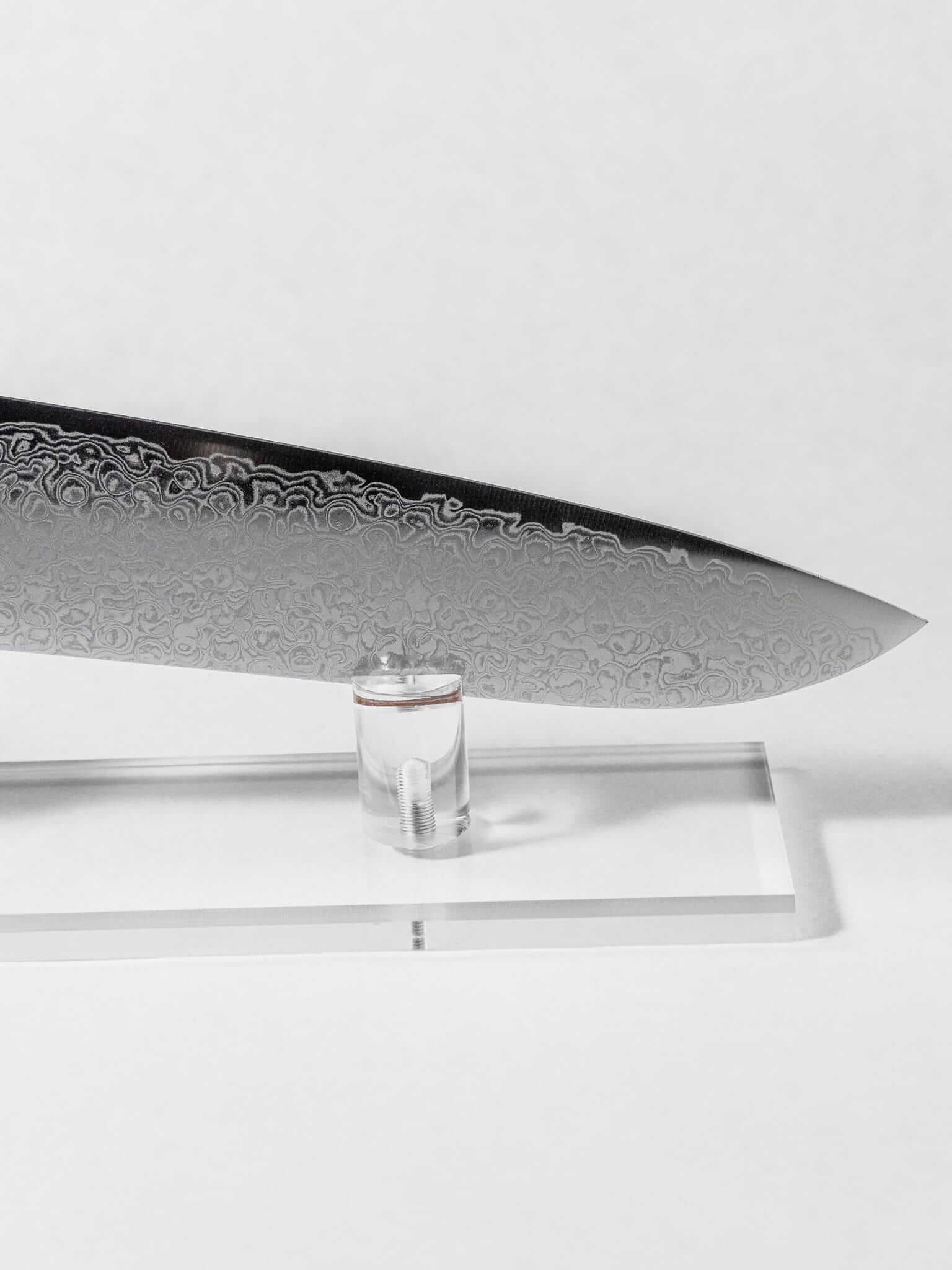 Close up of the stainless Damascus cladding pattern detail. Sharp tip of the Santoku against a white background.