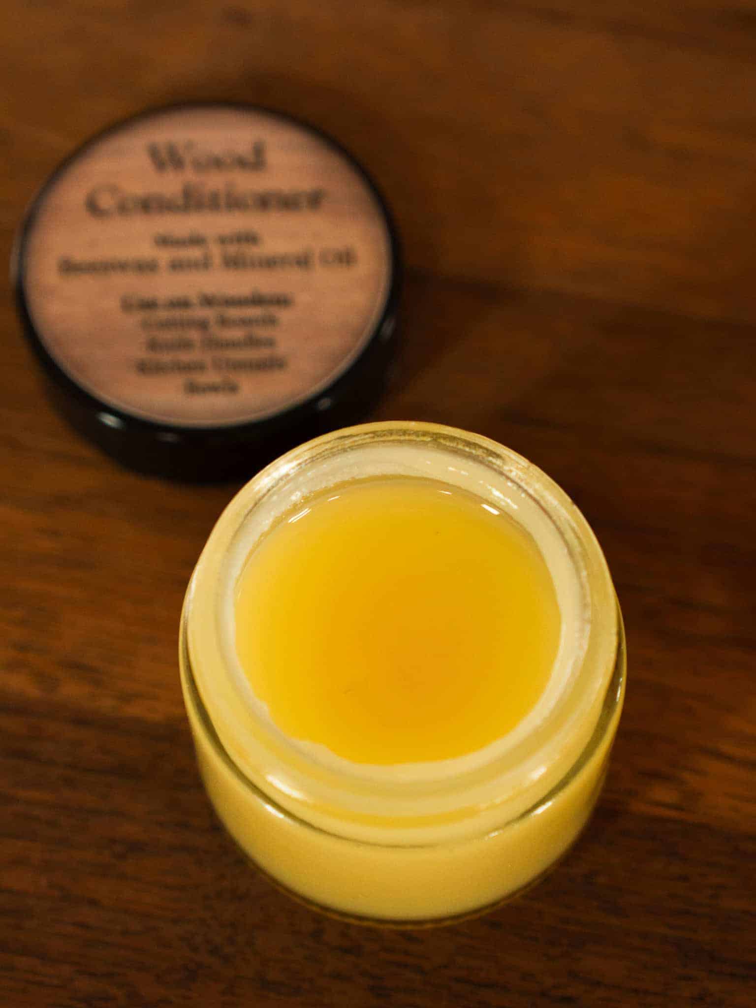 Close up of Lesley Morton wood conditioner made of beeswax and mineral oil on a wooden surface with a label in the background.