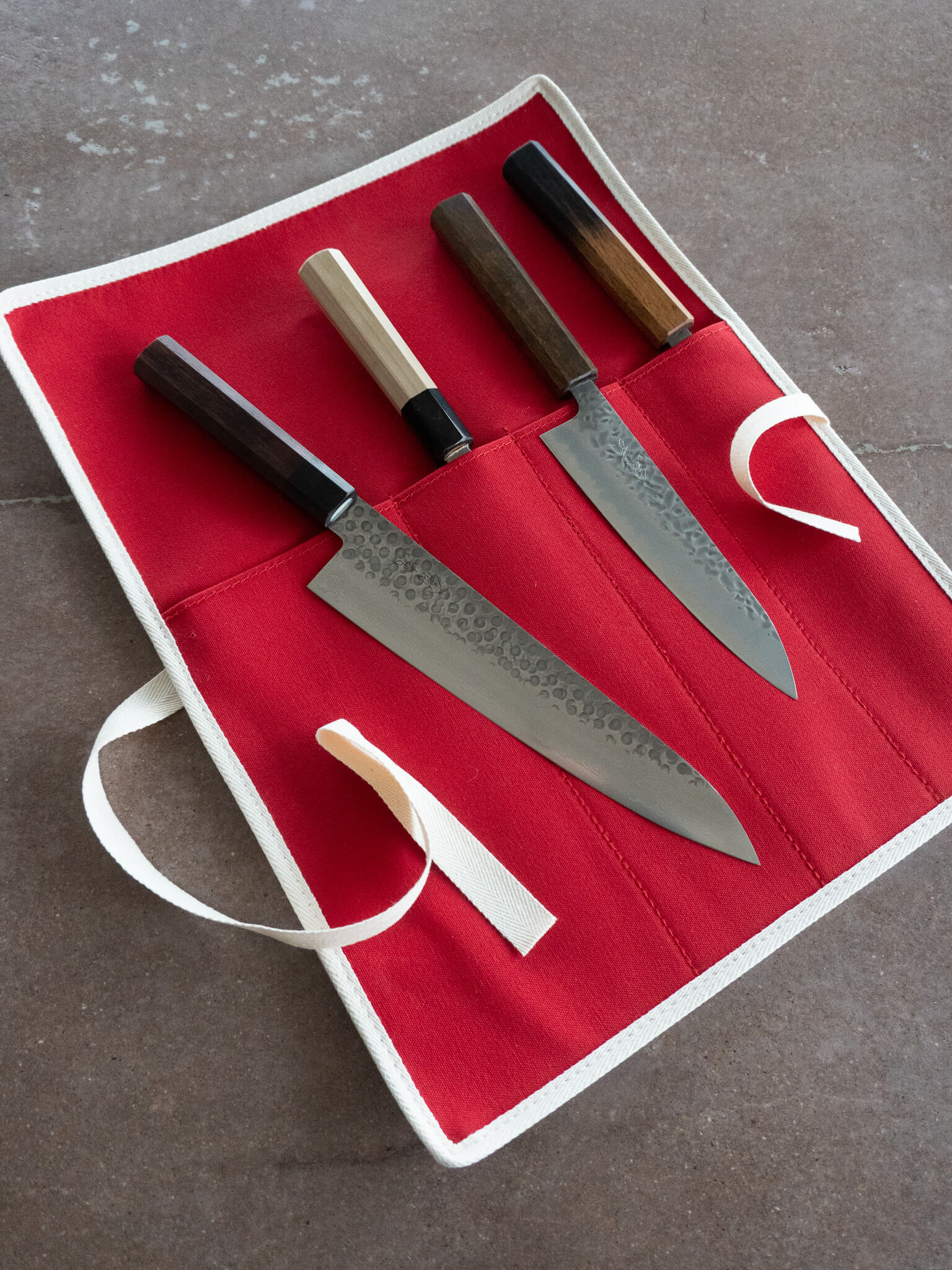 Canvas knife roll laid out with knives for size reference and storage layout. Canvas roll contains 4 slots for knives.