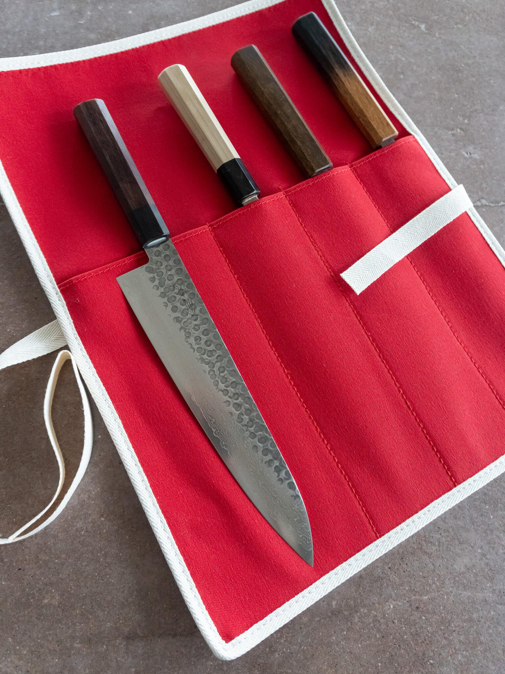 Bright red canvas knife roll with white piping used for safe transport during travel or kitchen storage.