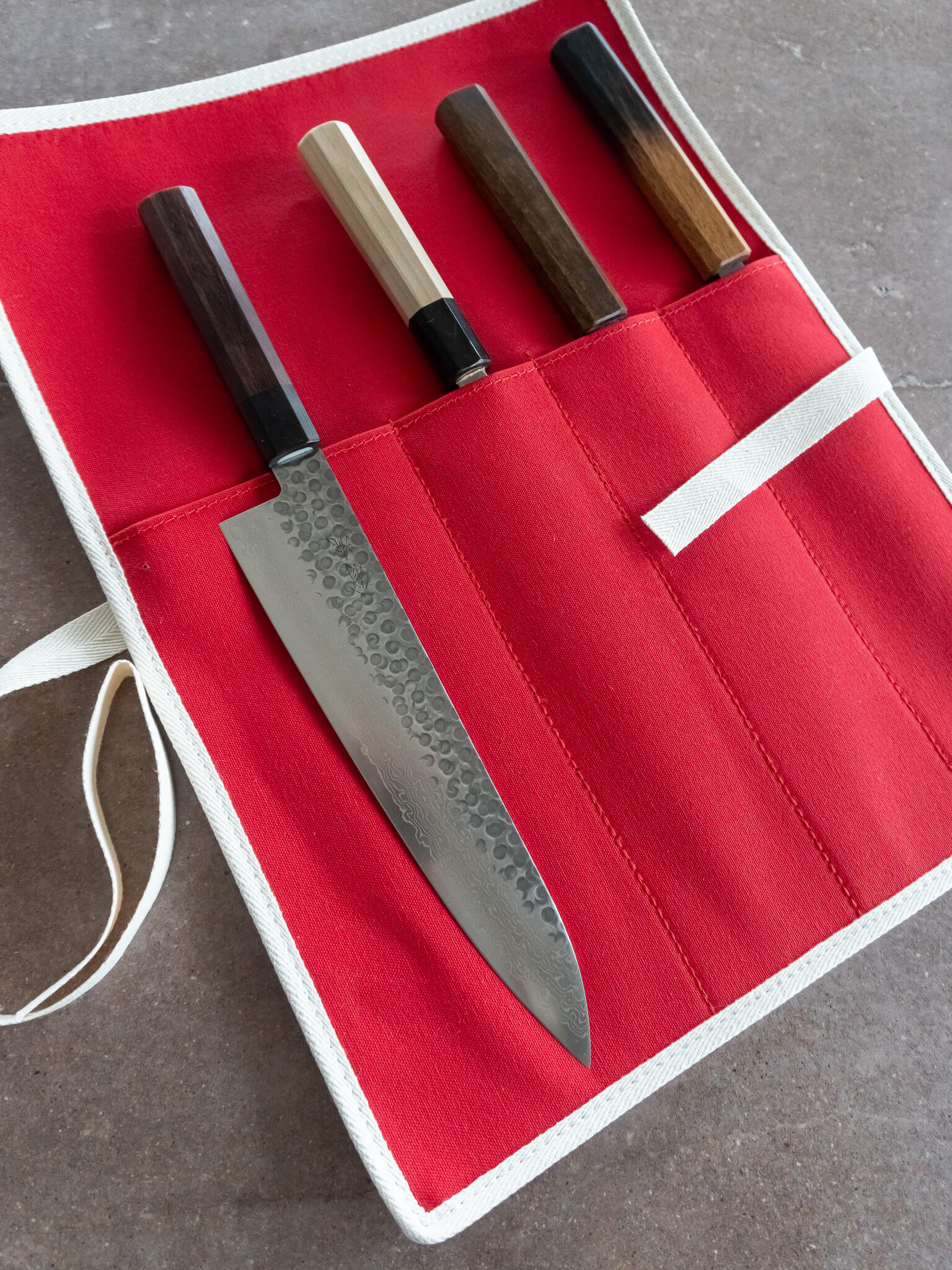Bright red canvas knife roll with white piping used for safe transport during travel or kitchen storage.