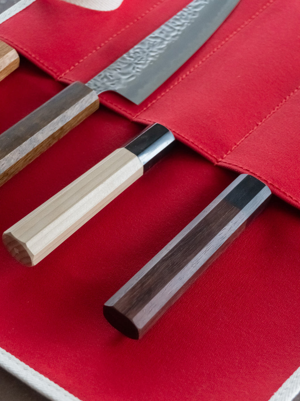 Unrolled red canvas knife roll showing multiple knife storage slots.
