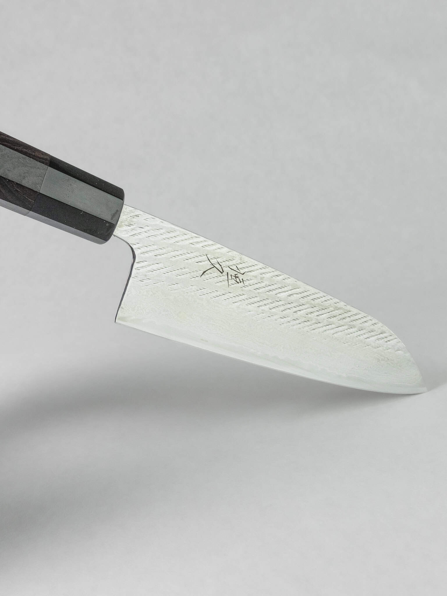 Japanese Santoku knife's unique Nawame textured pattern detail on a white background.
