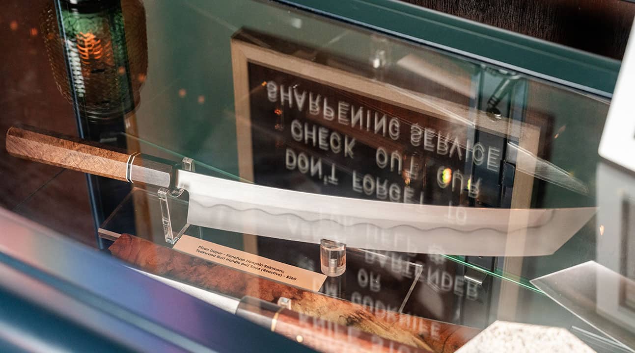 Large knife with wooden handle displayed in a glass case, with a sign in the background.