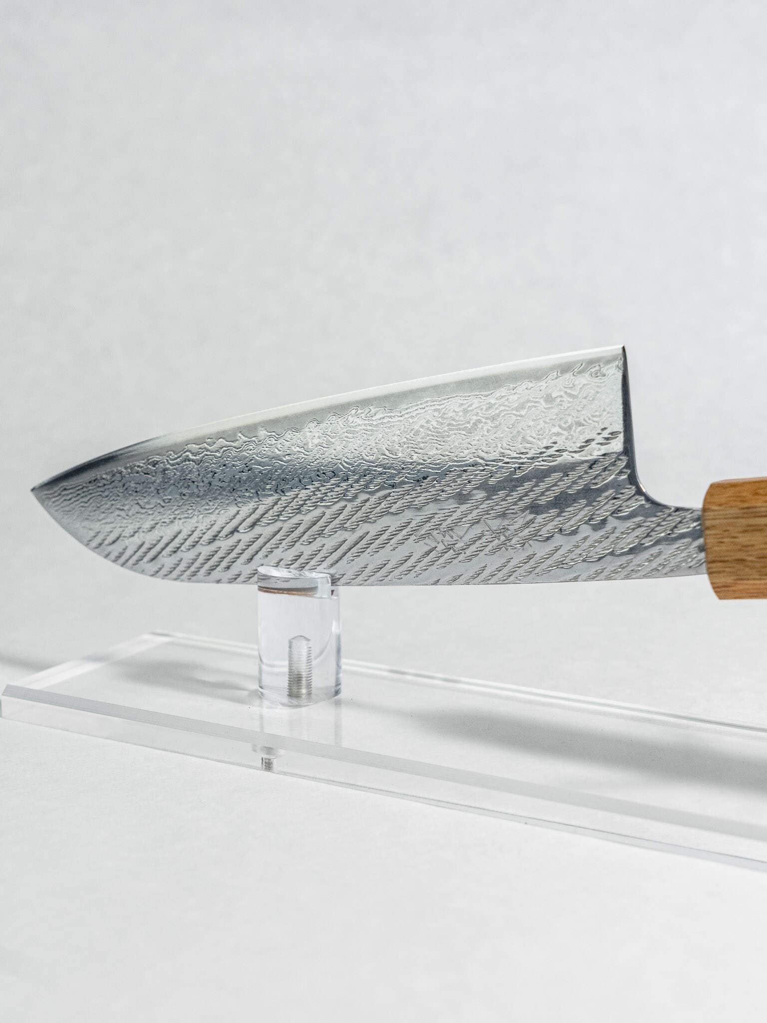 Chef's knife with a wooden handle on a clear stand against a white background. Handcrafted Santoku knife made in Sakai Japan.