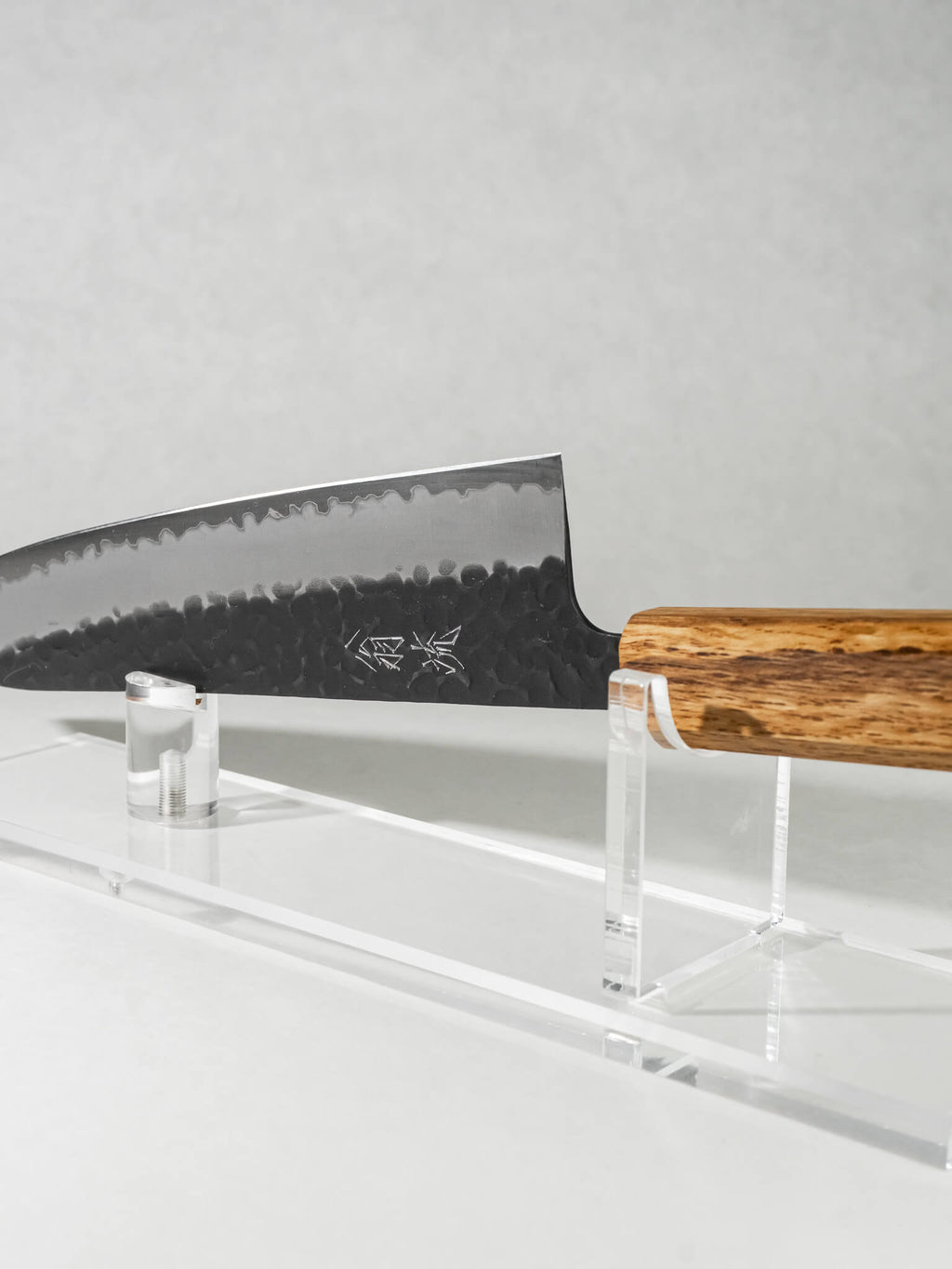 Close-up of OUL Gyuto 210mm blade showing hand-hammered tsuchime pattern and Aogami Super core with an octagonal darkened oak handle.