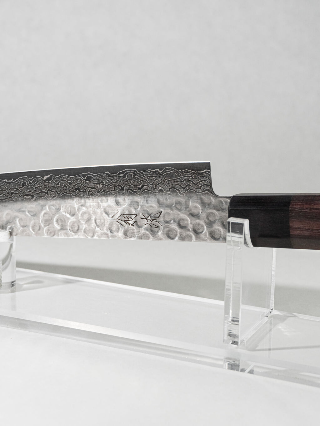 Close-up of the OUL Damascus Tsuchime Sujihiki knife, highlighting the hammered tsuchime finish, intricate Damascus layering, and balanced handle for precise slicing and control.