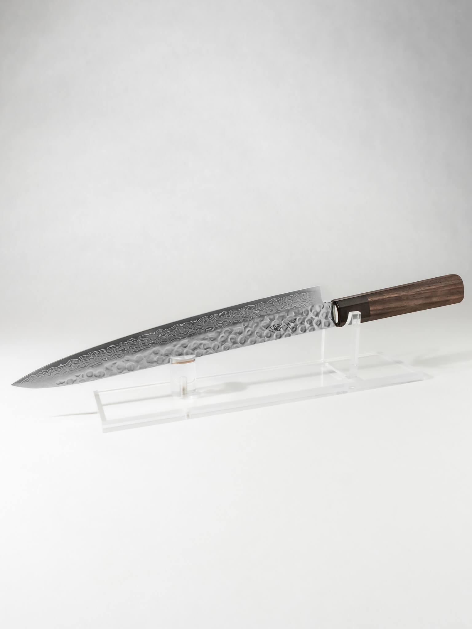 OUL Damascus Tsuchime Sujihiki or slicer knife with a long, slender blade ideal for precision slicing of fish, meat, and roasts. Features a hammered (tsuchime) finish for reduced food sticking and a beautiful layered Damascus pattern. Paired with a comfortable handle for balance and control, perfect for professional chefs and home cooking enthusiasts.