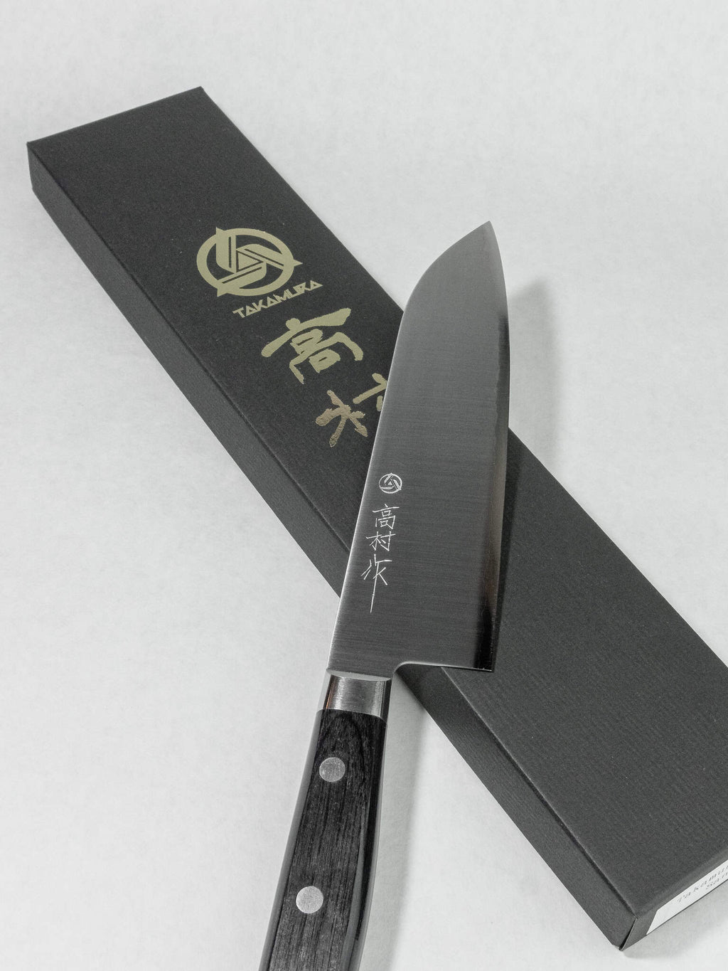 Stainless migaki polished finish on Takamura Santoku resting on a black box on a white background.
