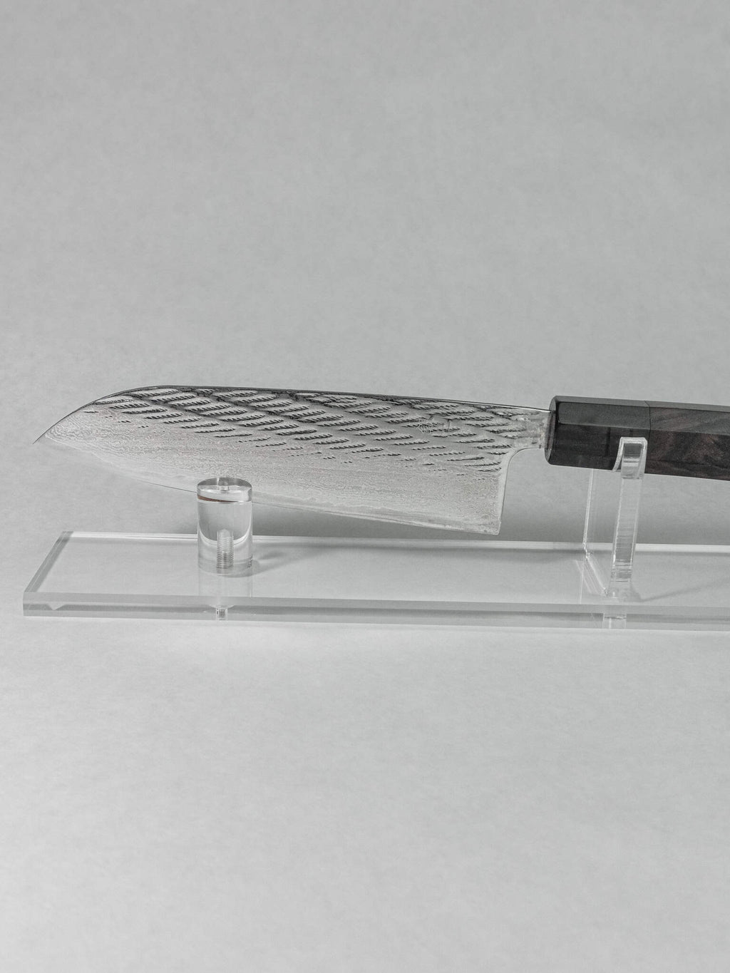 Santoku knife showing hammering detail on the side, on a stand against a gray background.