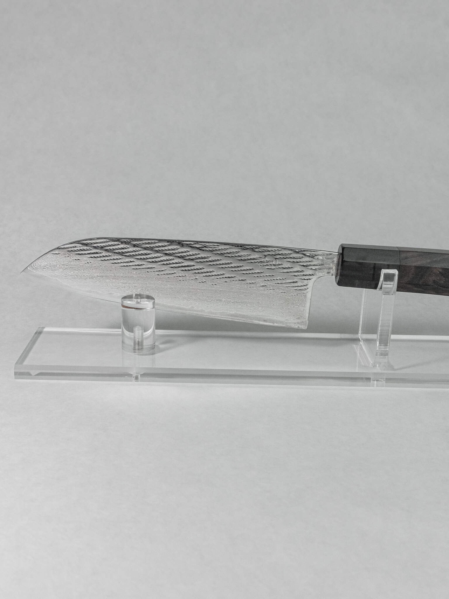 Santoku knife showing hammering detail on the side, on a stand against a gray background.